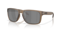 Oakley sunglasses with a matte taupe-brown frame and dark gray lenses, shown at a three-quarter angle on a white background with a soft reflection.