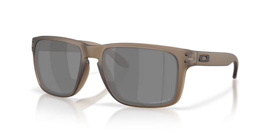 Oakley sunglasses with a matte taupe-brown frame and dark gray lenses, shown at a three-quarter angle on a white background with a soft reflection.