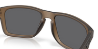 Close-up of a pair of sunglasses with a translucent brown frame and dark gray lenses, shown on a clean white background with a soft reflection.