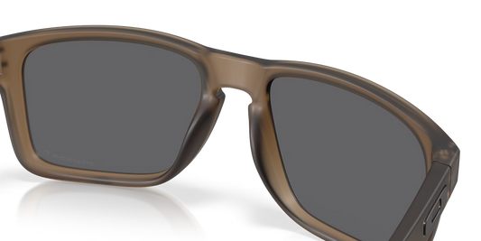 Close-up of a pair of sunglasses with a translucent brown frame and dark gray lenses, shown on a clean white background with a soft reflection.
