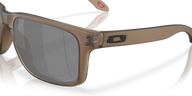 Oakley sunglasses with a translucent taupe-brown frame and dark gray lenses, shown on a clean white background with a soft reflection.