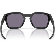 Black Oakley sunglasses with a matte black frame and dark gray lenses, shown from the front on a white background with a soft reflection.