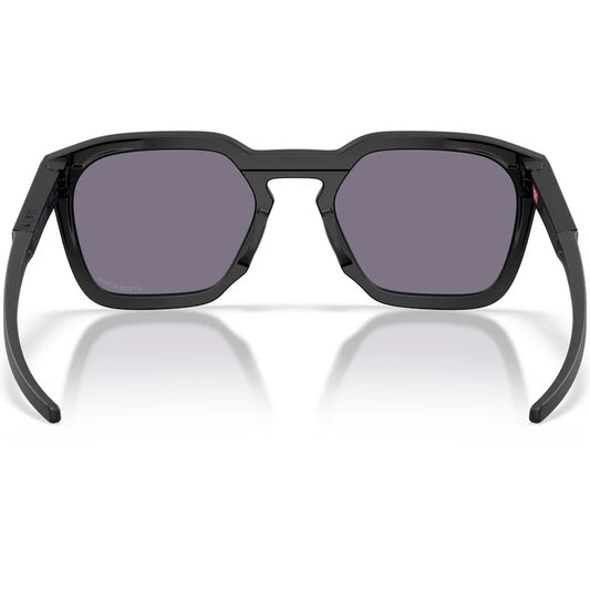 Black Oakley sunglasses with a matte black frame and dark gray lenses, shown from the front on a white background with a soft reflection.