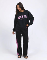 Woman wearing a black 'FOXWOOD' sweatshirt and pants with pink stripes on a white background