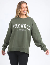 Woman wearing a green sweatshirt with 'FOXWOOD' printed on it against a white background