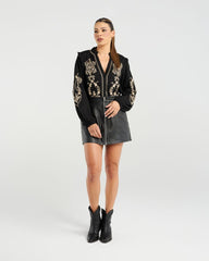 Woman wearing a black blouse with gold patterns, black leather skirt, and black boots on a white background