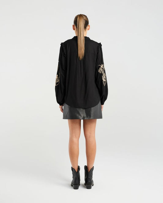 Person wearing a black outfit with floral embroidery on sleeves against a white background