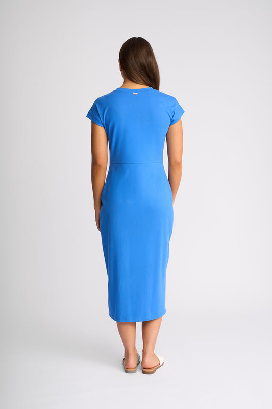 A woman viewed from the back wearing a bright blue short-sleeve midi dress, standing against a light gray studio background.