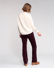 Person wearing a white sweater and burgundy pants on a light gray background