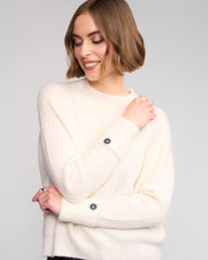 Woman wearing a cream-colored sweater with buttons on a gray background