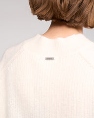 Person wearing a white sweater with a brand logo on a light gray background