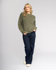Woman wearing a green sweater and dark blue jeans on a white background