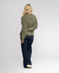 Person wearing a green sweater and dark blue jeans on a white background