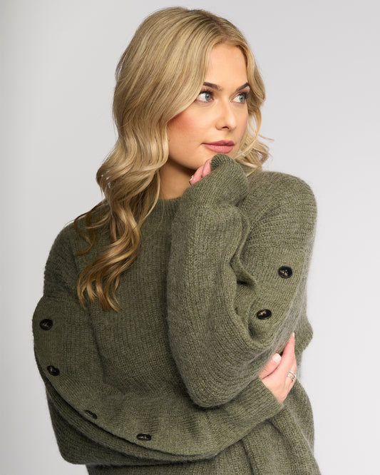 Woman wearing a green knitted sweater with buttons on a plain background