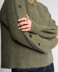 Green knitted sweater with button details on a plain background