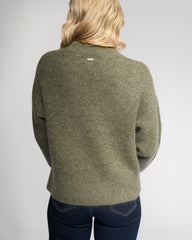 Person wearing a green sweater with a visible brand logo on a gray background