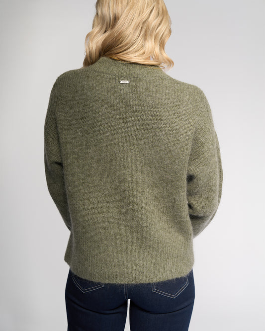 Person wearing a green sweater with a visible brand logo on a gray background