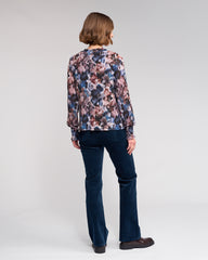 Woman wearing a floral blouse and dark jeans on a plain background