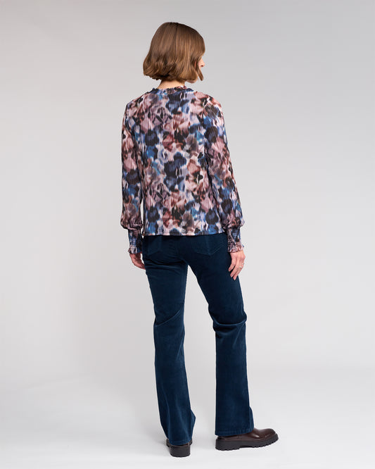 Woman wearing a floral blouse and dark jeans on a plain background