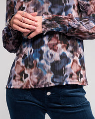 Person wearing a patterned shirt with long sleeves and dark pants on a light gray background