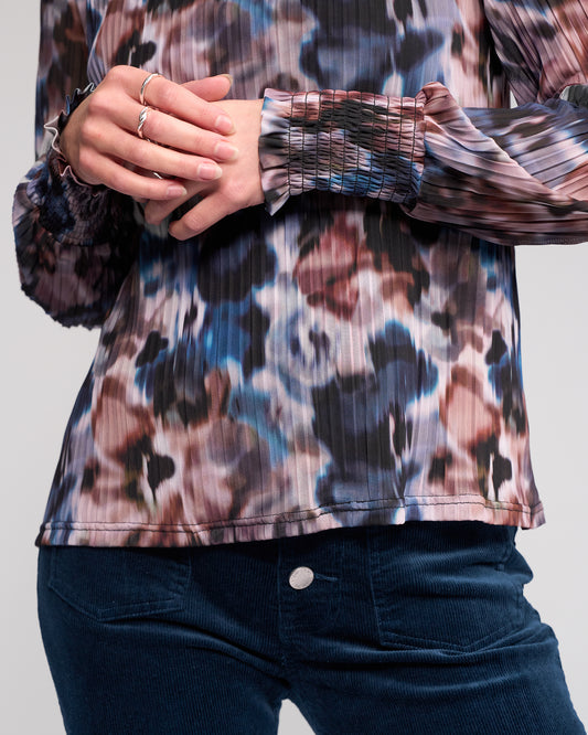 Person wearing a patterned shirt with long sleeves and dark pants on a light gray background