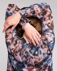 Person wearing a patterned garment with their hands covering their face on a plain background