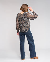 Person wearing a patterned blouse and blue jeans on a white background