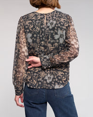 Person wearing a sheer floral blouse with long sleeves on a plain background