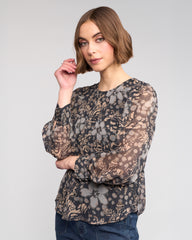 Woman wearing a sheer floral blouse with long sleeves on a plain background