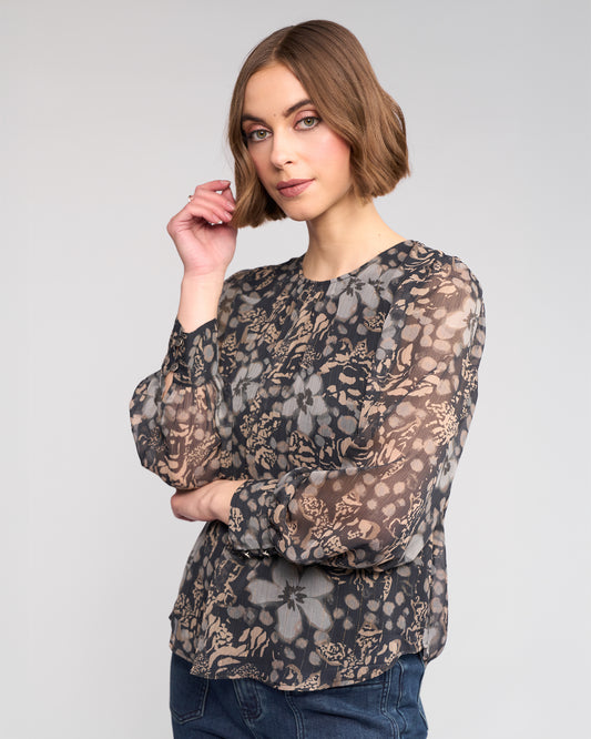 Woman wearing a sheer floral blouse with long sleeves on a plain background