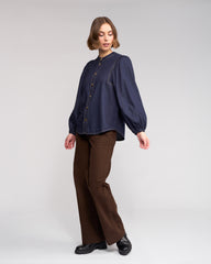 Woman wearing a navy blue blouse and brown pants on a white background