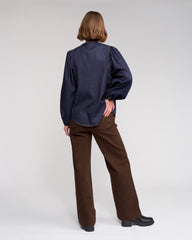 Person wearing a navy blue blouse and brown pants on a white background