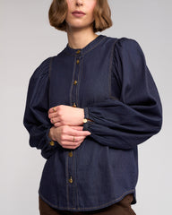 Person wearing a dark blue blouse with puffed sleeves on a plain background