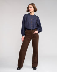 Woman wearing a navy blouse with brown pants on a white background