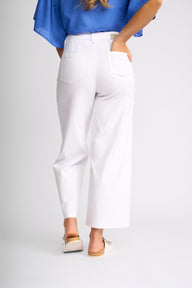 White cropped wide-leg pants shown on a model from the back, paired with a blue blouse and beige slide sandals, against a light gray studio background.