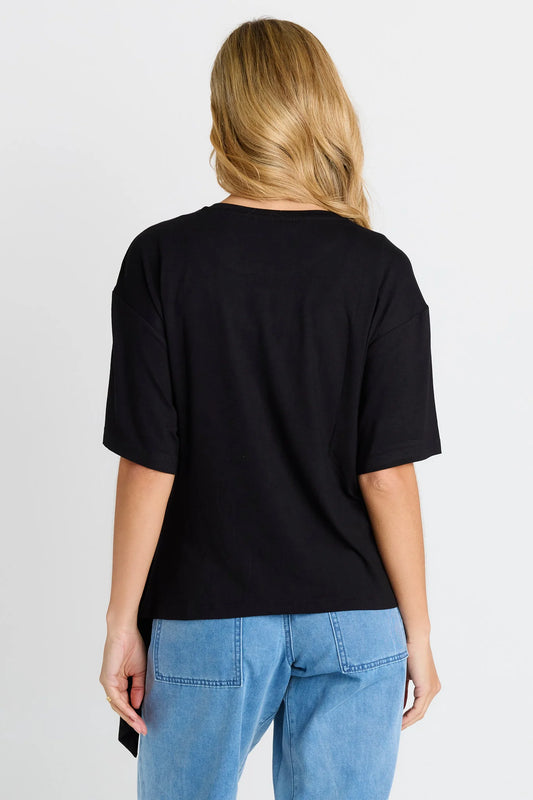 A woman viewed from the back wearing a black short-sleeve t-shirt and light blue jeans against a plain light gray background.