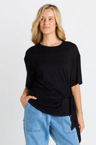 Woman wearing a black top and blue jeans on a light gray background