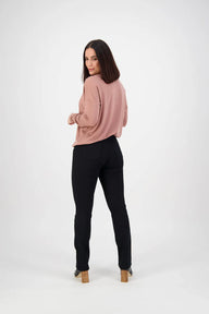 Woman wearing a pink sweater and black pants on a white background