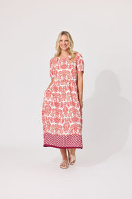 A woman modeling a short-sleeve midi dress with a pink and white floral pattern and a solid magenta border, standing against a light gray studio background.