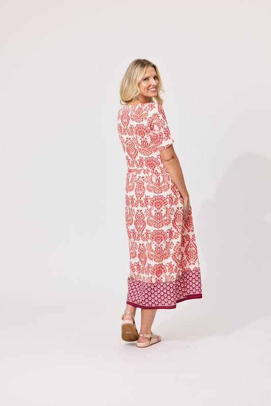 A woman modeling a short-sleeved midi dress with a red and white floral pattern, shown from a three-quarter back view against a plain white studio background.