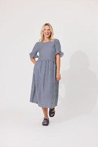 A woman modeling a blue and white vertically striped midi dress with puff sleeves, standing against a plain white studio background.