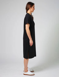 Woman wearing a black dress with white sneakers on a plain background