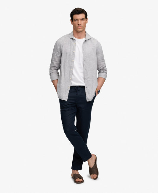 Man wearing a light gray shirt, white undershirt, dark pants, and sandals on a white background