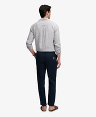 A man viewed from the back wearing a light gray long-sleeve button-up shirt and dark navy trousers, standing against a plain light gray studio background.