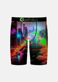 Ethika branded boxer briefs featuring a vibrant, neon-lit cyberpunk cityscape print with glowing green lights, pink clouds, and dark skyscrapers, shown against a light gray background.