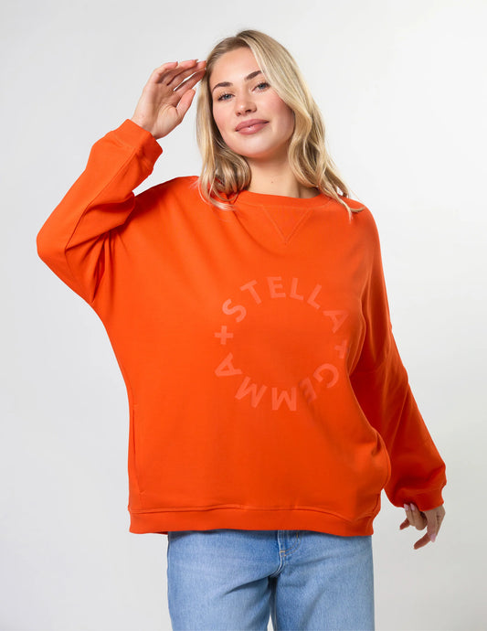 Person wearing an orange sweatshirt with 'Stella + Gemma' logo on a white background