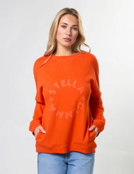 Woman wearing an orange sweatshirt with 'Stella + Gemma' logo on a white background