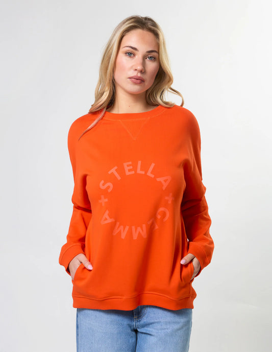 Woman wearing an orange sweatshirt with 'Stella + Gemma' logo on a white background