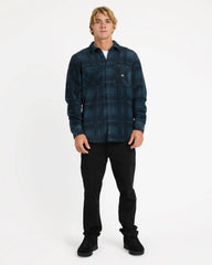 Man wearing a blue plaid shirt and black pants on a white background
