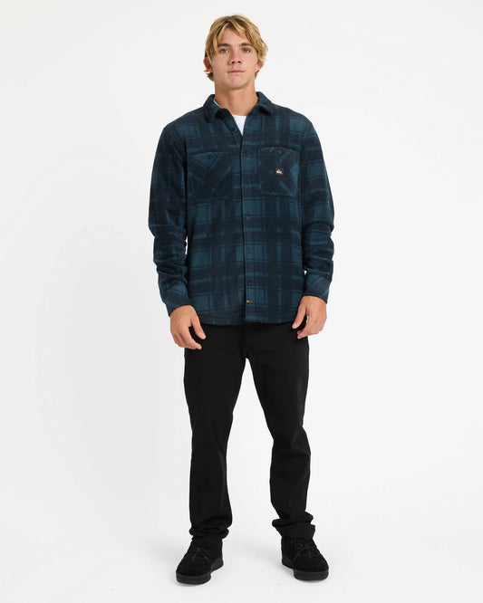 Man wearing a blue plaid shirt and black pants on a white background